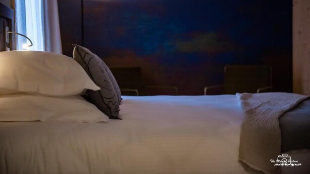 A hotel room with a bed, pillows, a bedside lamp, and a wall mural. - Logis Hotel Le Chalet Altitude (Pierre-Percée)