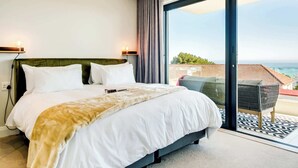 Quarto moderno com uma cama grande, duas luminárias de cabeceira e vista para o oceano através de uma porta de vidro deslizante.