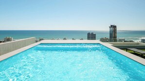 Piscina infinita no terraço com vista desimpedida do oceano e horizonte urbano.
