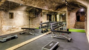 Academia com paredes de tijolo, tetos com espelhos e diversos equipamentos de exercício.