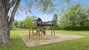 A wooden swing set with a bench and a small shelter, surrounded by grass and trees. - Mammoth Pond - Mammoth Cave Family Retreat - Playground Sleeps 6 (Cave City)