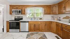 A kitchen with wooden cabinets, stainless steel appliances, a window with blinds, and a marble floor. - Mammoth Pond - Mammoth Cave Family Retreat - Playground Sleeps 6 (Cave City)