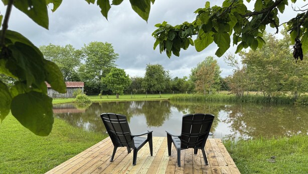 A wooden deck with two chairs facing a calm pond, surrounded by lush greenery and trees. - Mammoth Pond - Mammoth Cave Family Retreat - Playground Sleeps 6 (Cave City)
