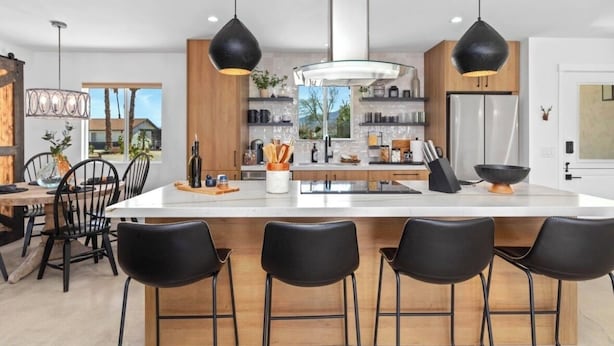 Une cuisine moderne dotée d’un îlot central, de tabourets de bar noirs et de luminaires suspendus.