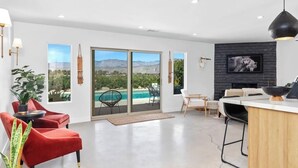 Un salon moderne doté d’une grande porte-fenêtre coulissante donnant sur une piscine, d’une cheminée et d’un coin repas.