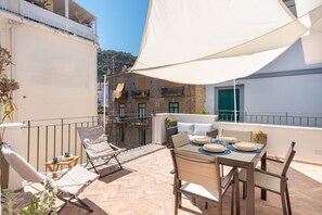 A terrace with a table set for dining, lounge chairs, and a large white canopy.