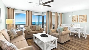 A spacious living room with a white coffee table, beige sofas, and a dining area with white chairs. - Latitude 29 Unit 19 (Panama City Beach)