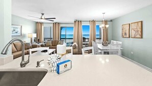 A modern hotel room with a kitchen area, dining space, and a balcony with a view of the ocean. - Latitude 29 Unit 19 (Panama City Beach)