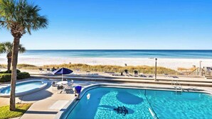 A pool area with a view of the beach, lounge chairs, and umbrellas. - Latitude 29 Unit 19 (Panama City Beach)