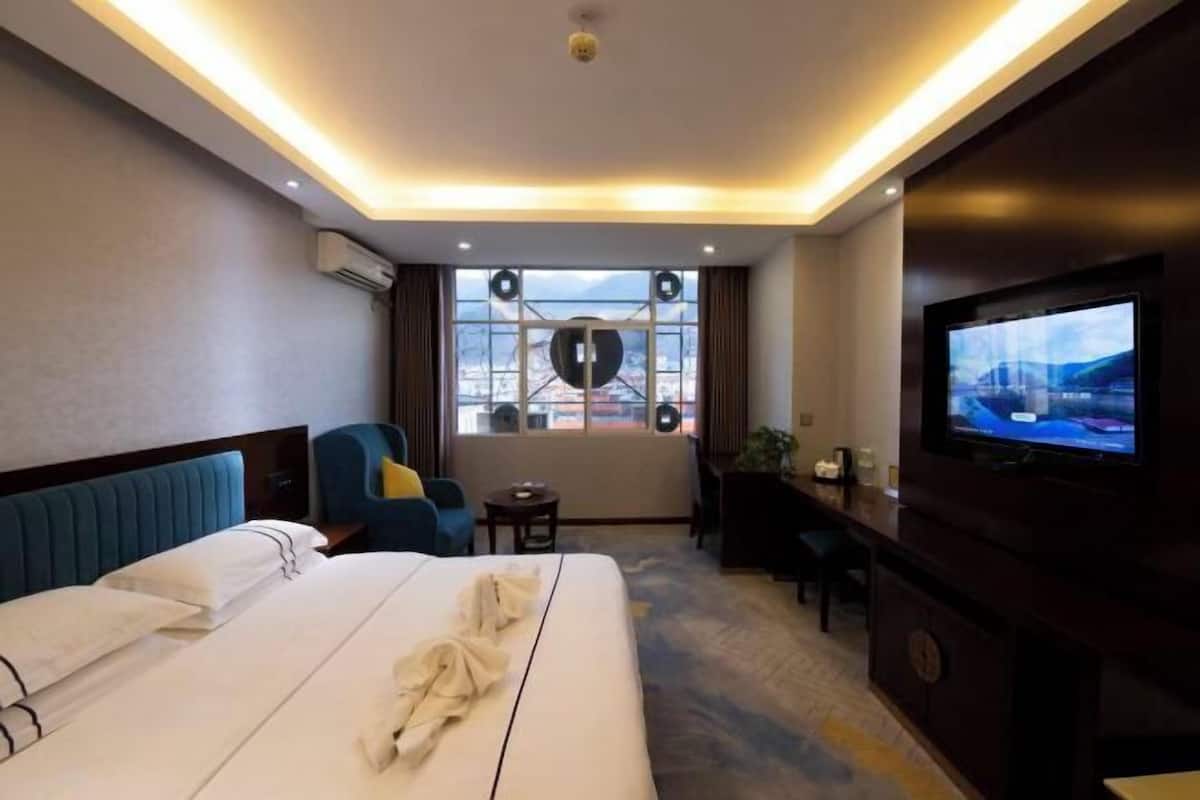 A hotel room with a bed, a TV, a desk, and a window with a city view.