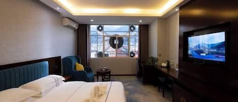 A hotel room with a bed, a TV, a desk, and a window with a city view.