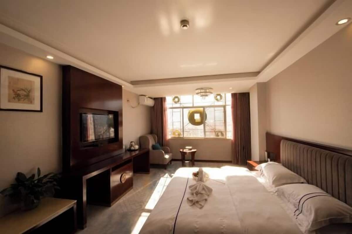 A hotel room with a large bed, a television, a desk, and a window with curtains.