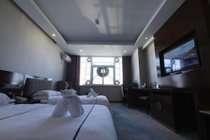 Habitación de hotel con dos camas, un escritorio, un televisor y un ventanal con vistas.