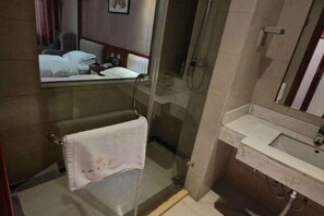 Un baño de hotel con cabina de ducha de vidrio, lavamanos y espejo.