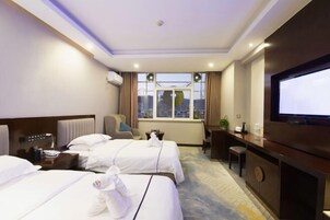 Quarto de hotel com duas camas, uma mesa, uma televisão e janela com vista para a cidade.