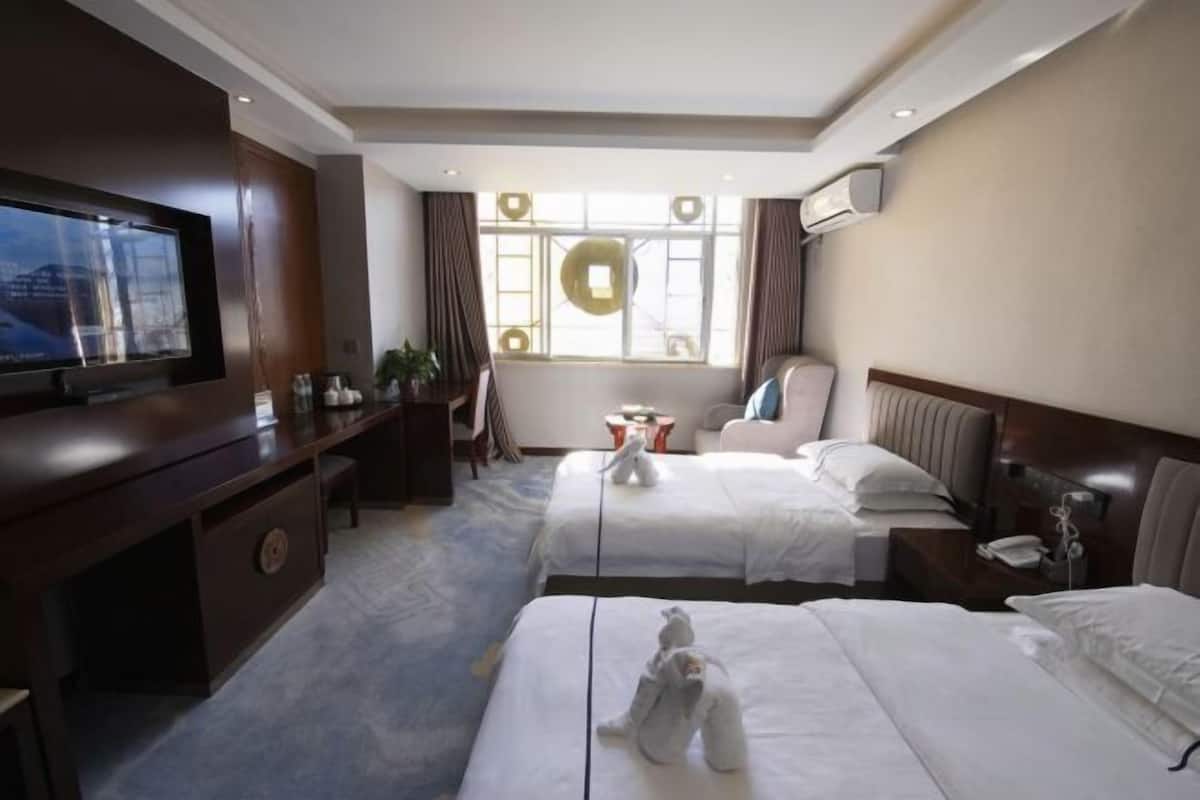 A hotel room with two beds, a TV, a desk, and a window with curtains.