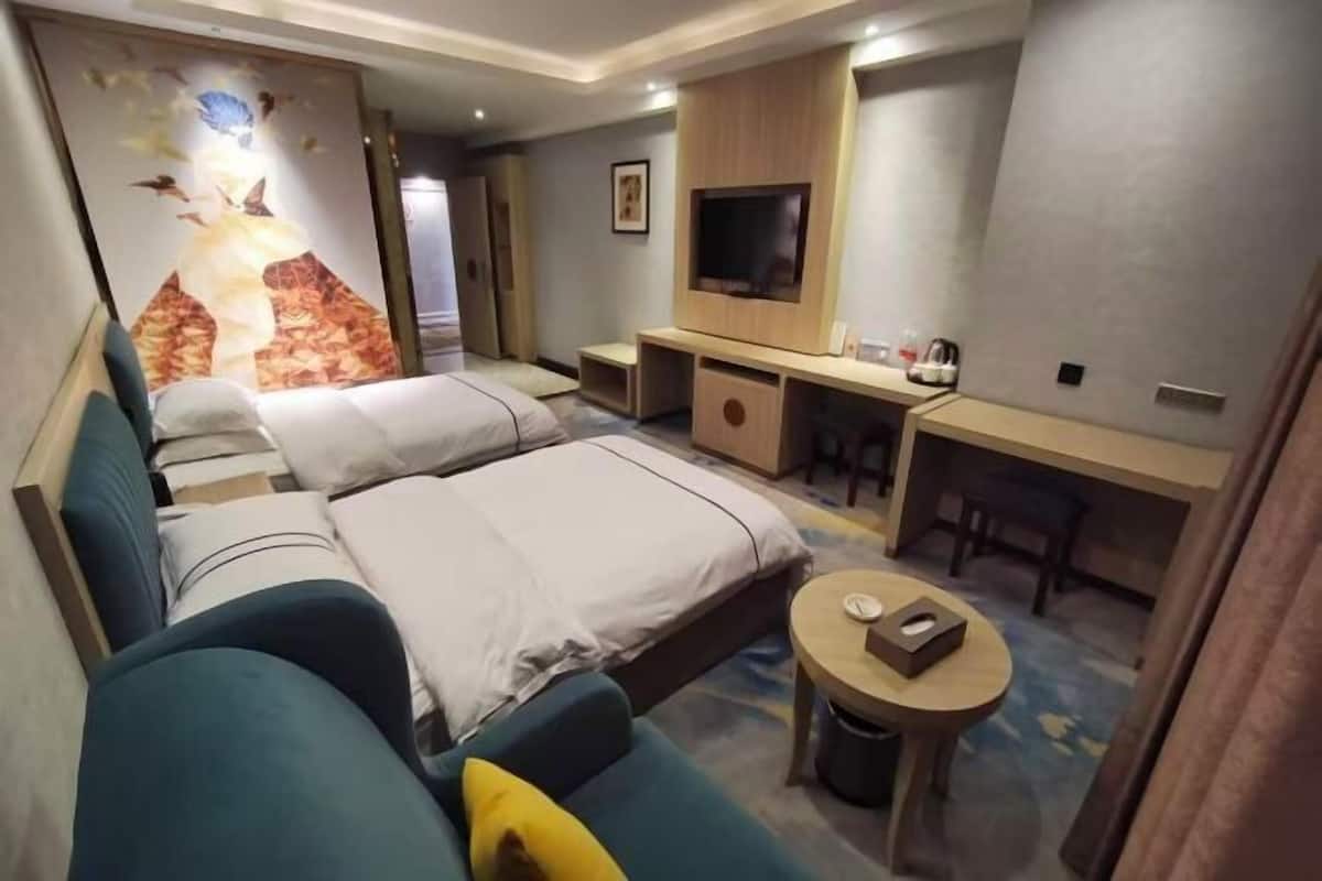 A hotel room with two beds, a sofa, a TV, a desk, and a small table.