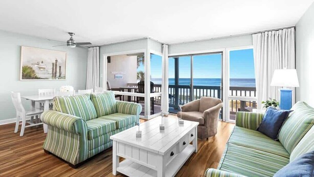 A living room with striped sofas, a white coffee table, and a view of the ocean.