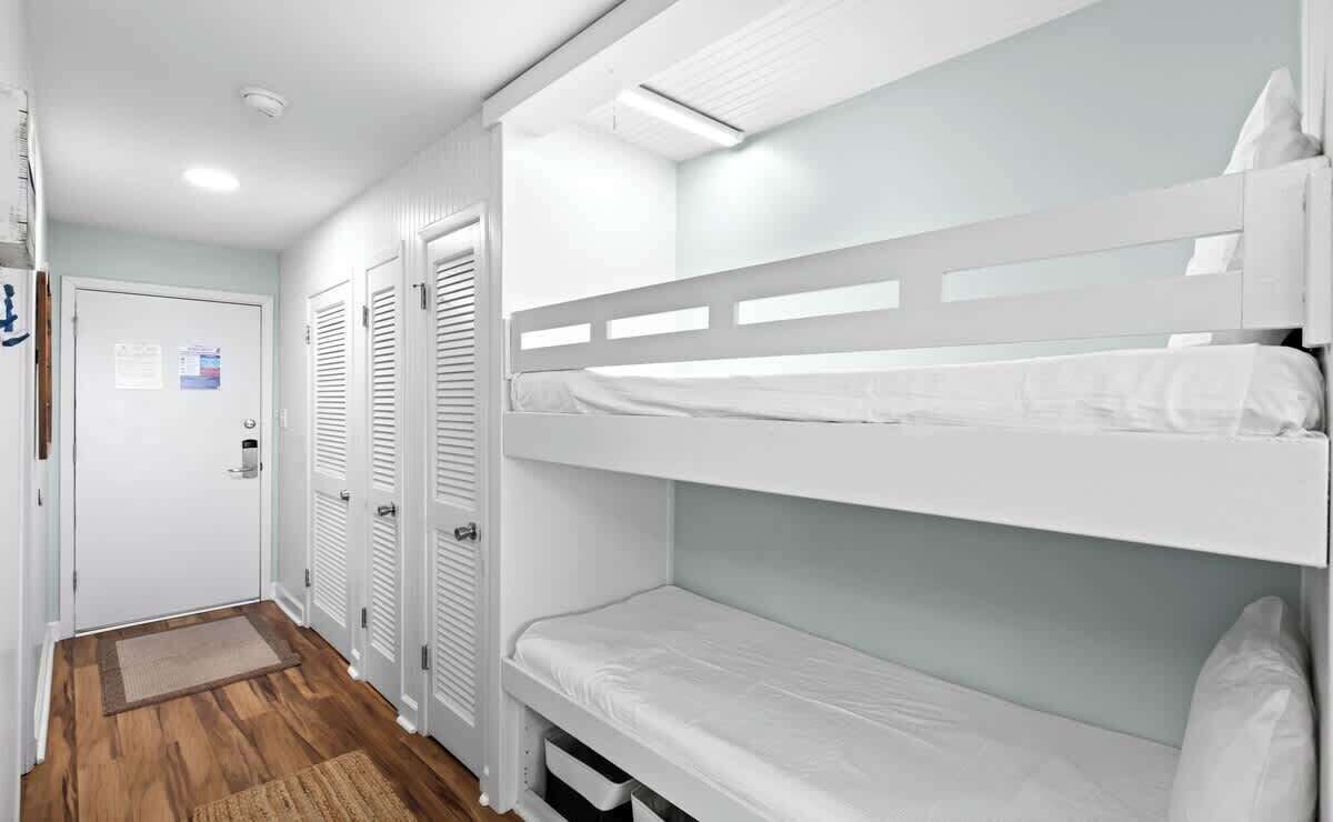 A bunk bed room with a wooden floor, white walls, and a door with a notice.