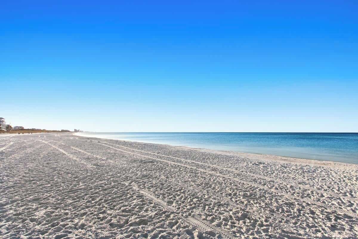 Una amplia playa de arena con marcas de neumáticos visibles, que se extiende hacia el océano.