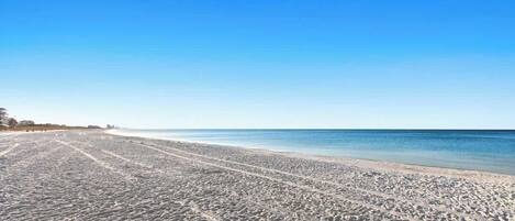 Una amplia playa de arena con marcas de neumáticos visibles, que se extiende hacia el océano.
