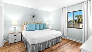 A bedroom with a bed, nightstands, a window with curtains, and a decorative wall piece.