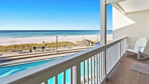 A balcony with a pool, beach view, and white chairs.