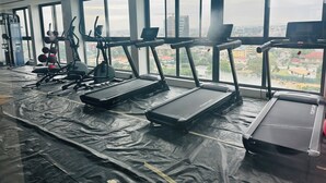 Une salle de sport équipée de tapis de course, de ballons d’exercice et d’un rameur, avec de grandes fenêtres donnant sur un paysage urbain.