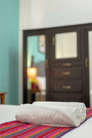 A neatly folded white towel on a bed with a colorful striped bedspread.