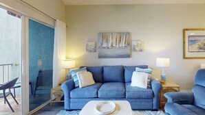 A living room with a blue sofa, two side tables with lamps, a white coffee table, and a glass door leading to an outdoor area.