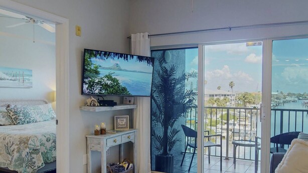 Una sala de estar con televisión, una cama, un balcón con sillas y vistas al puerto deportivo.