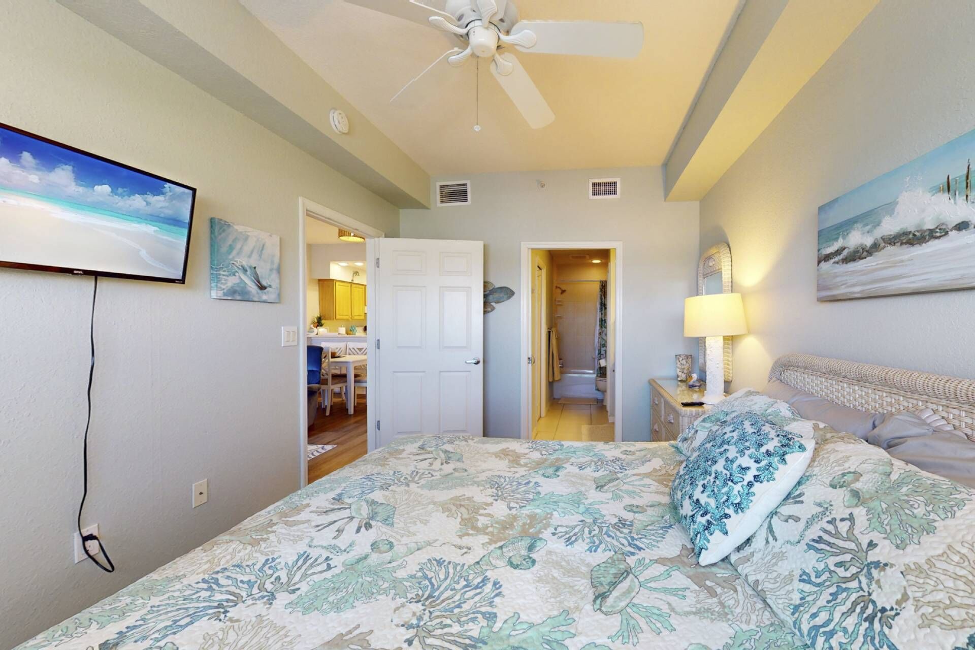 A bedroom with a bed, a ceiling fan, a painting, and a view of the bathroom.