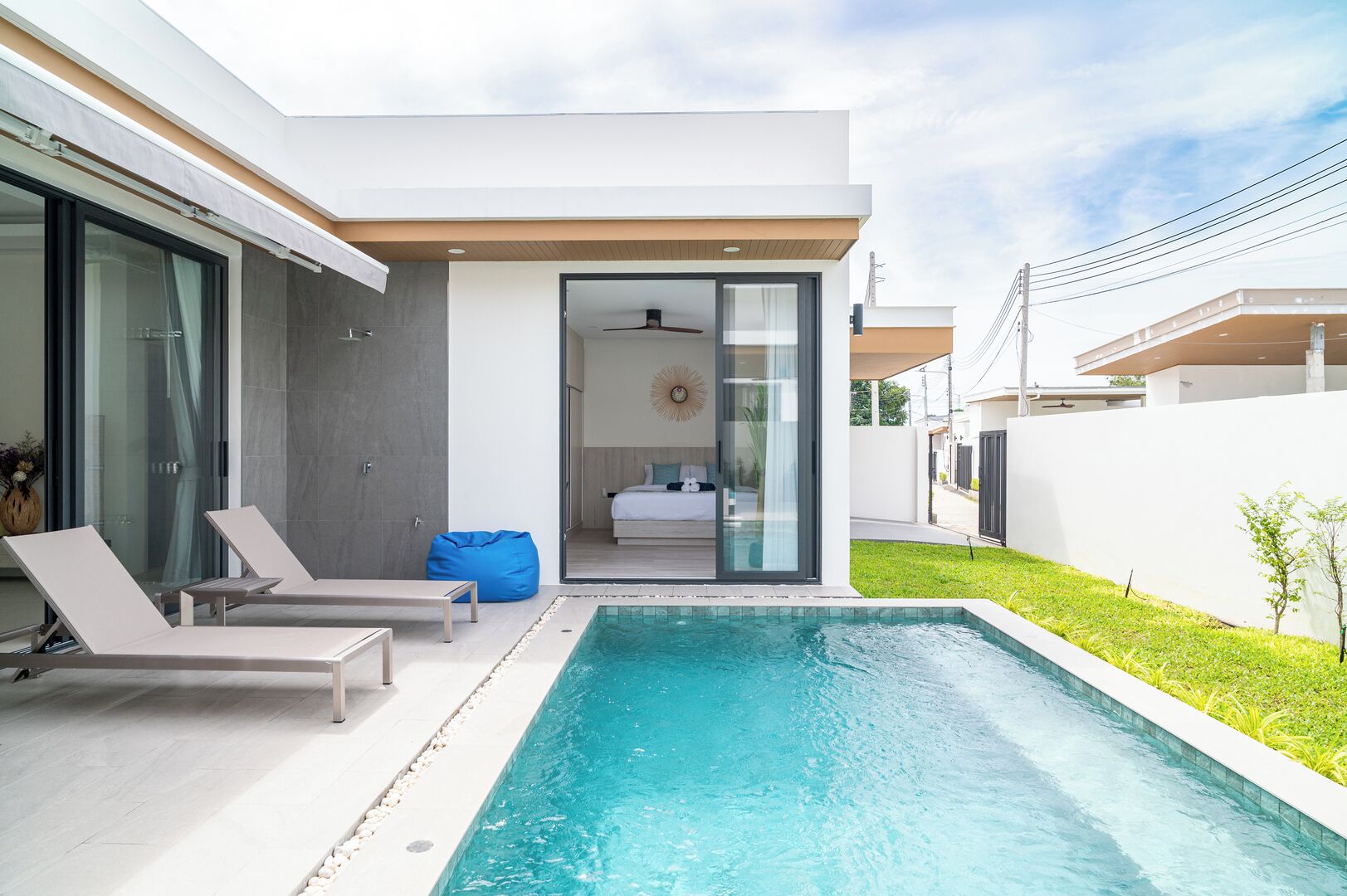 Una casa moderna con piscina, un ventanal que da a un dormitorio y un pequeño jardín.