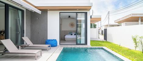 Una casa moderna con piscina, un ventanal que da a un dormitorio y un pequeño jardín.