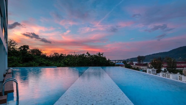 An infinity pool with a tiled floor and metal railings, surrounded by greenery and buildings, under a sunset sky. - Sea View Suite C64 in Oceana near Beach (Kamala)