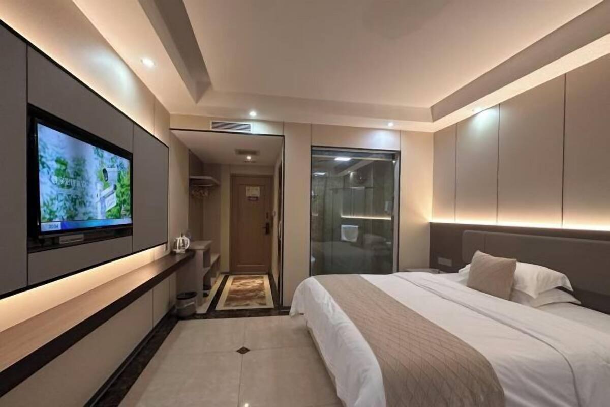 Ein modernes Hotelzimmer mit einem großen Flachbildfernseher, einem Bett mit einer beigen Decke und einer Duschkabine aus Glas.