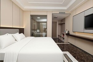 Ein Hotelzimmer mit einem großen Bett, einem Flachbildfernseher, einer Minibar und einem durch eine Glastür einsehbaren Badezimmer.