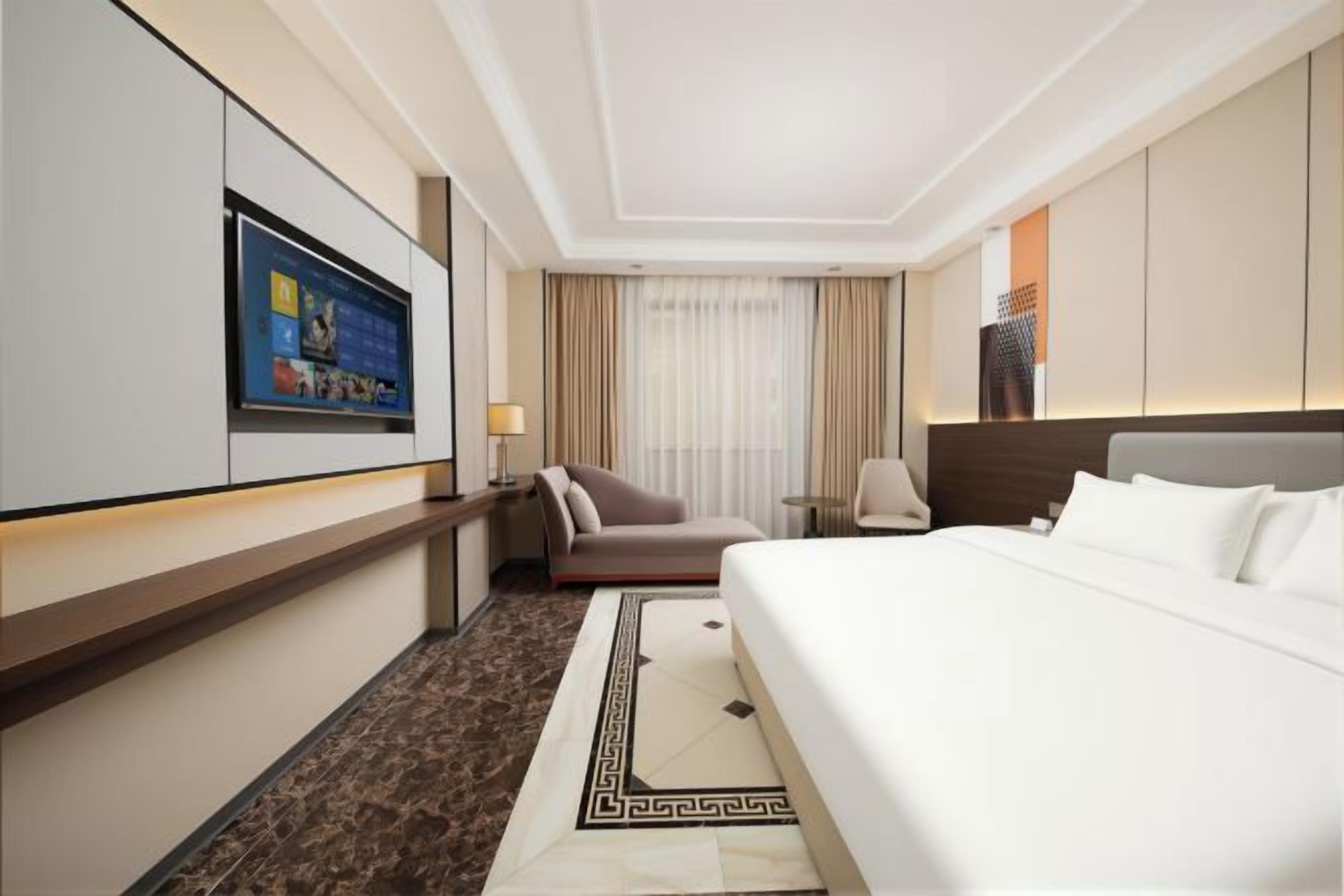 A hotel room with a bed, a desk, a chair, a TV, and a window with curtains.