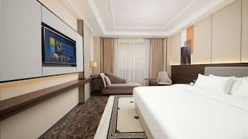 A hotel room with a bed, a desk, a chair, a TV, and a window with curtains.