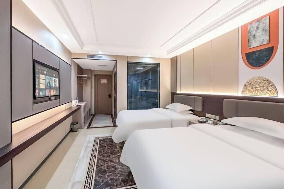 Ein Hotelzimmer mit zwei Betten, einem Fernseher, einem Kleiderschrank und einem durch eine Glastür einsehbarer Badezimmer.