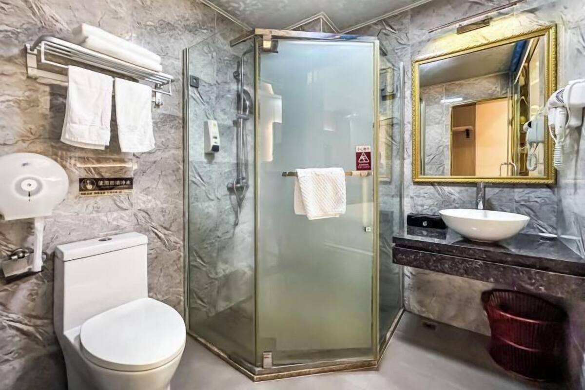 A bathroom with a glass-enclosed shower, a toilet, a sink with a marble countertop, and a mirror with a gold frame.