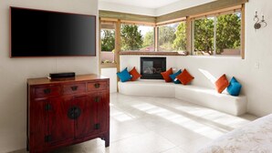 A room with a large flat-screen TV mounted on the wall, a wooden cabinet, a white sofa with colorful cushions, and a fireplace. - Mystic View: A 3-bedroom, 3-bath house in West Sedona close to trails & dining (Sedona)