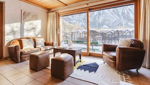 A cozy living room with a leather sofa, a coffee table, and a view of a snowy landscape through large windows.