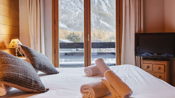 A hotel room with a bed, a television, and a window with a view of a snowy landscape.