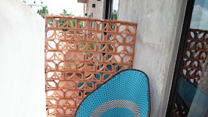 Una silla azul de mimbre en un patio con baldosas, una cerca de madera decorativa y un vidrio.