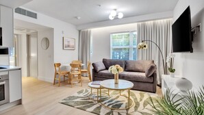 A modern living room with a sofa, coffee table, and chairs, a kitchen area, and a large window with curtains. - Vonder Miami Beach - Unit 1 (Miami Beach)