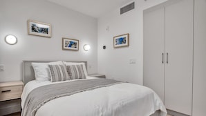 Quarto com uma cama grande, mesas de cabeceira, guarda-roupa e luminárias fixadas na parede.