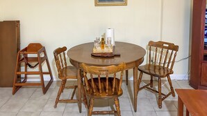 Et spiseområde med et rundt træbord, fire træstole, en lille træskammel og en bakke med glas og en flaske.