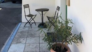 A covered outdoor seating area with two chairs and a table, a potted plant, and a metal plaque on the wall.