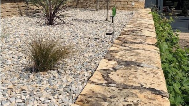 A stone pathway leading to a building with a stone facade and green shutters.